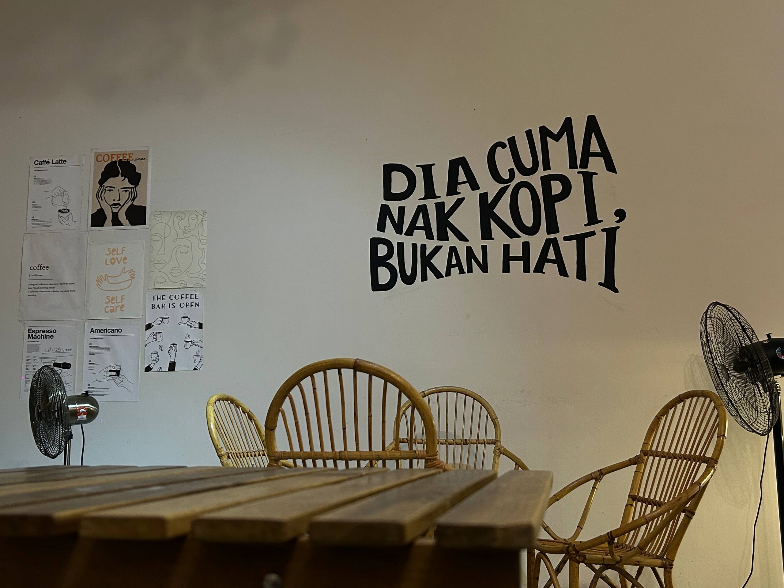 Rattan chairs and wooden tables beneath the Kopi & Bulan wall phrase