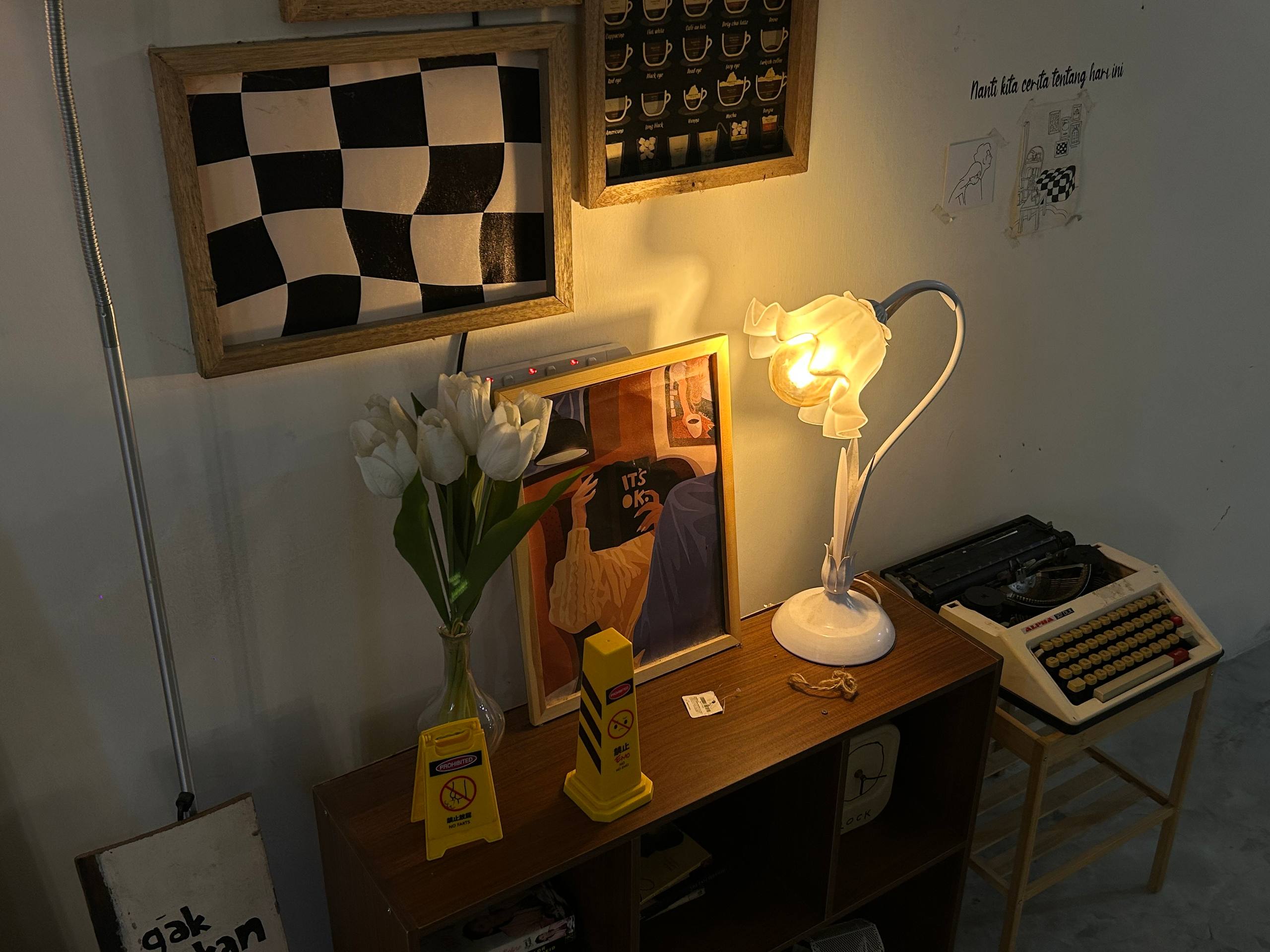 Warm café corner with framed checkerboard art, flowers, lamp and typewriter